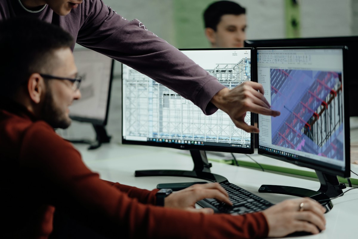Design colleagues reviewing a digital building model and technical drawings on two monitors