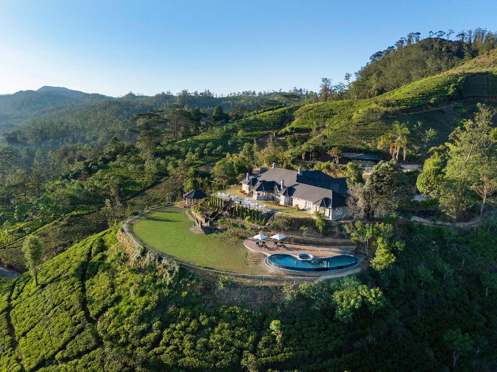 Elevated view of a pitched-roof building and gardens nestled into green highland slopes